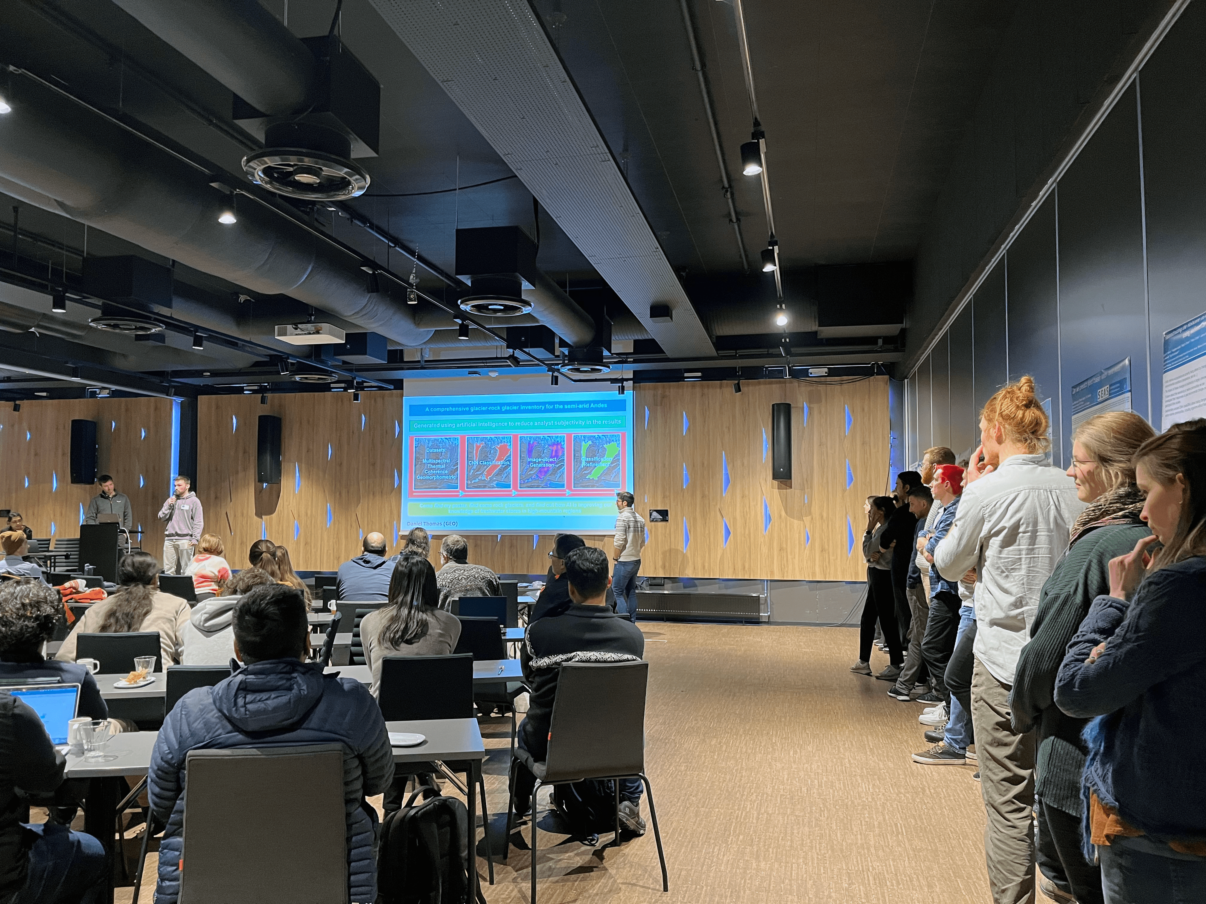 Scientist lining up against a wall covered with scientific posters, and watching a science presentation